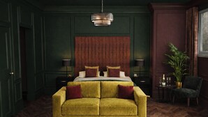 Ein Zimmer mit einem großen Bett, einer Couch, Holzboden, einer Wandleuchte und einem Topfpflanzen.