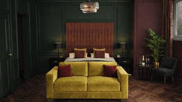 A room with a large bed, a sofa, a wooden floor, a wall-mounted light fixture, and a potted plant.