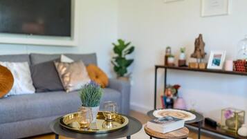 Una sala de estar moderna con un sofá gris, una mesita de centro con una bandeja y una pequeña mesita auxiliar con un libro.