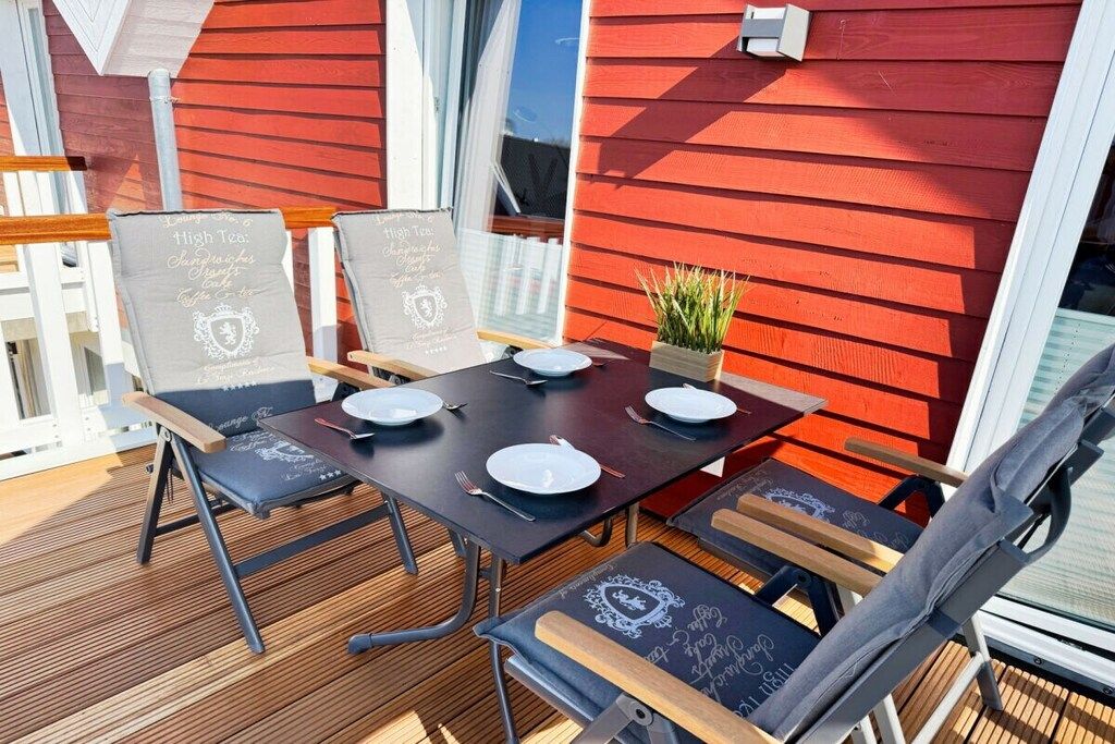 An outdoor dining area with a wooden deck, metal chairs, and tables set for two.