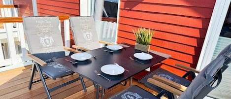 An outdoor dining area with a wooden deck, metal chairs, and tables set for two.