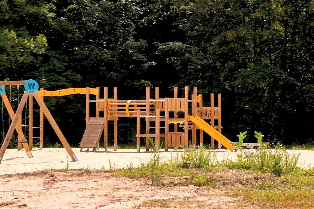 A wooden playground structure with a slide and climbing elements, surrounded by trees.