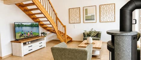 A living room with a wooden staircase, a television, a sofa, a coffee table, and a stone fireplace.