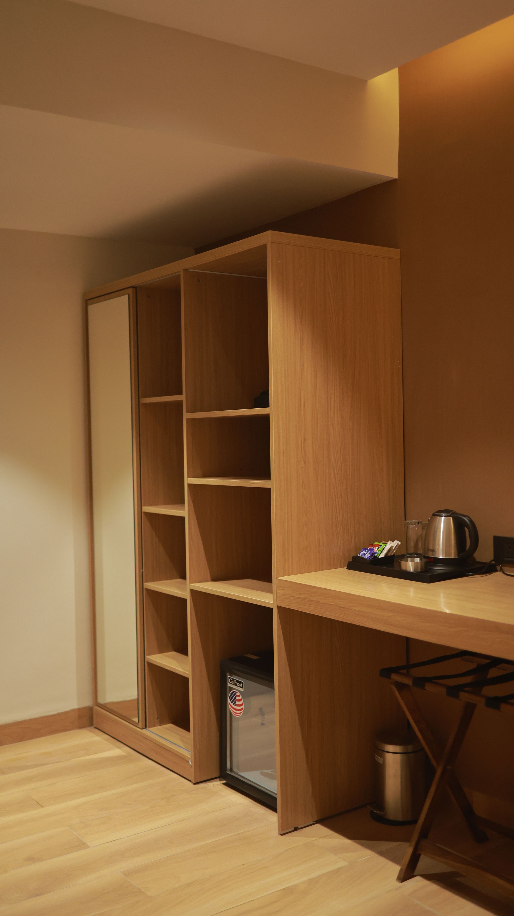 Ein Holzkoffer mit offenen Regalen, ein kleiner Kühlschrank und ein Wasserkocher auf einem Tisch.