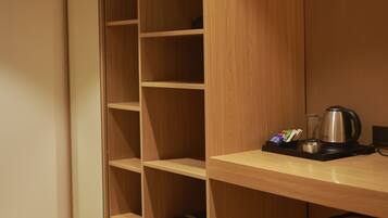 Un armario de madera con estantes abiertos, un refrigerador pequeño y una tetera sobre una mesa.
