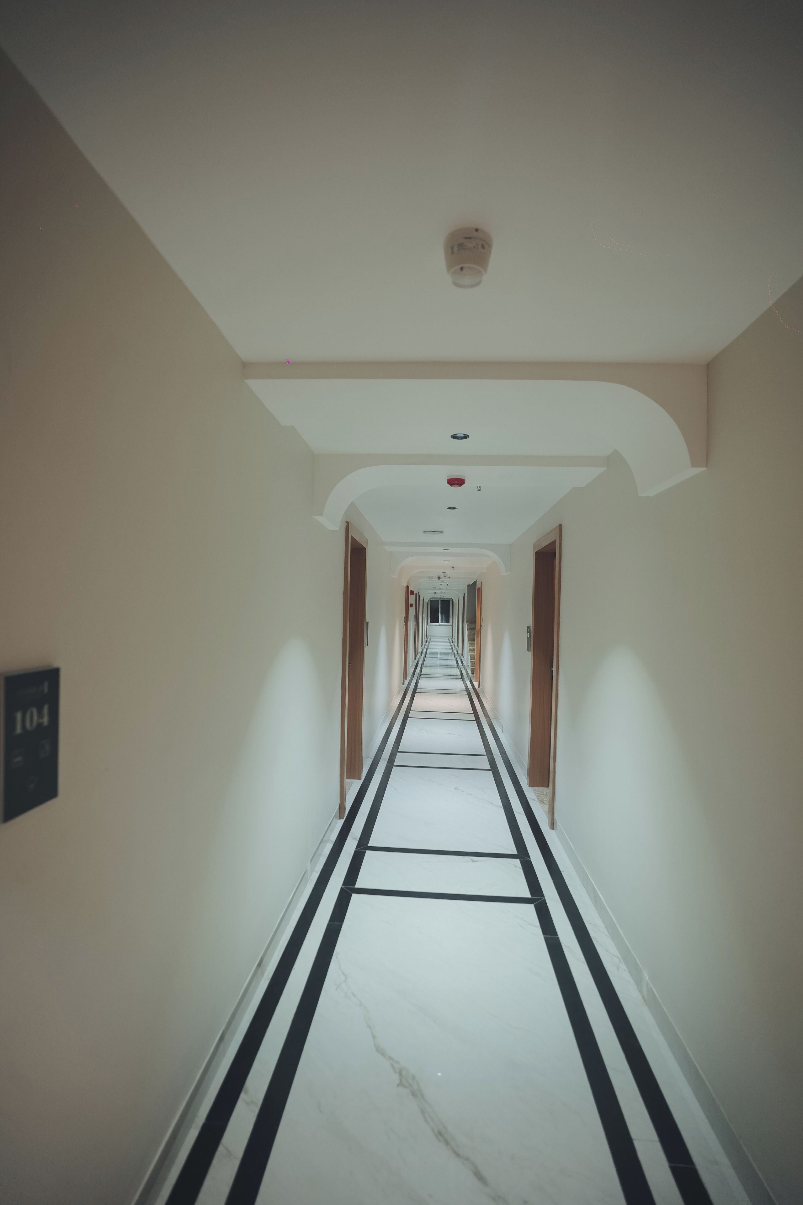 A long, narrow hotel corridor with a marble floor, white walls, and doors on both sides.