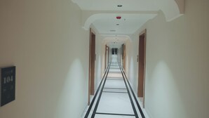 Un lungo e stretto corridoio d'albergo con pavimento in marmo, pareti bianche e porte su entrambi i lati.