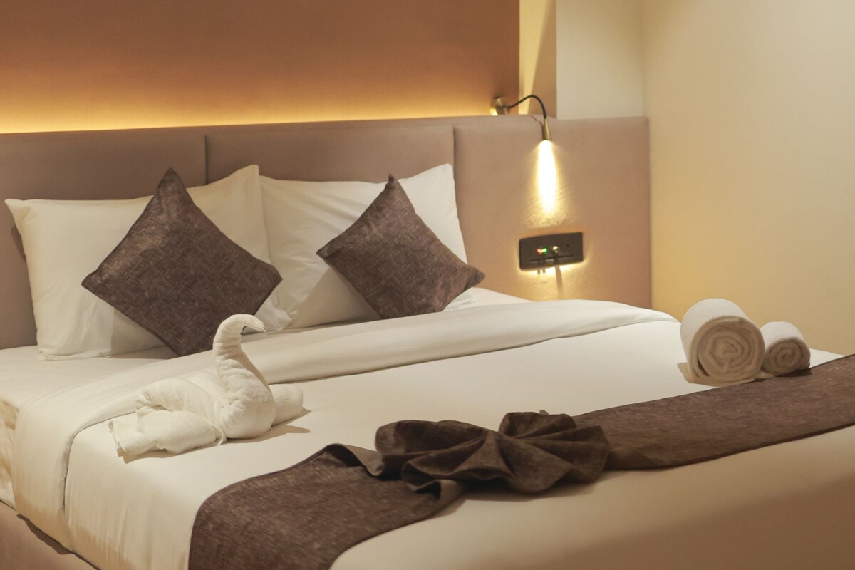 A hotel room with a large bed, a headboard with integrated lighting, and a bedside table with a lamp.