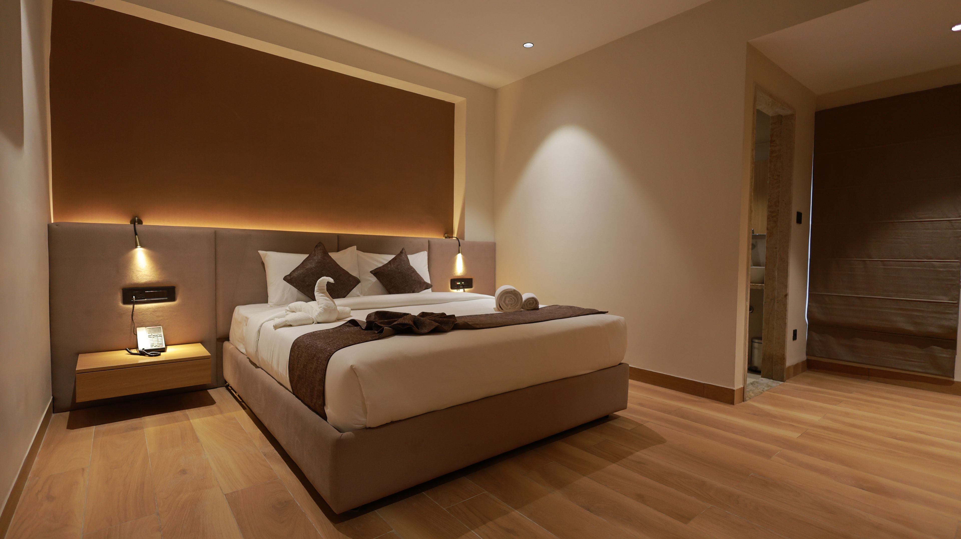 A modern bedroom with a large bed, bedside lamps, and a wooden floor.