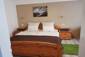 A bedroom with a wooden bed, two bedside tables, a green rug, and a wall-mounted picture. - Holiday apartment with 1 bedroom (Brodenbach)
