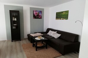Un saló amb un sofà negre, una taula petita, un armari i dos quadres penjats a la paret.