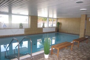 An indoor swimming pool with clear glass walls, wooden benches, and potted plants. - Residence Naturdüne Holiday Apartment No. 5 (Cuxhaven Duhnen)