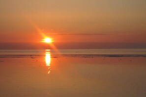 Ein Sonnenuntergang über einem Strand, das ruhige Wasser spiegelt die Sonne wider.