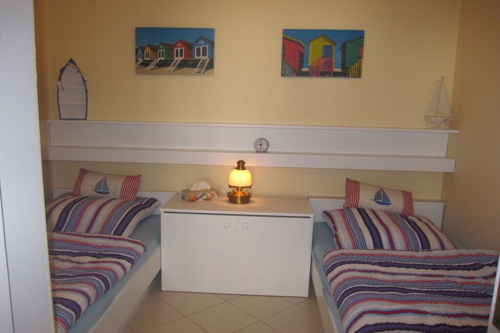 Ein Zimmer mit zwei Betten, einem Nachttisch mit Lampe und zwei Bildern an der Wand.