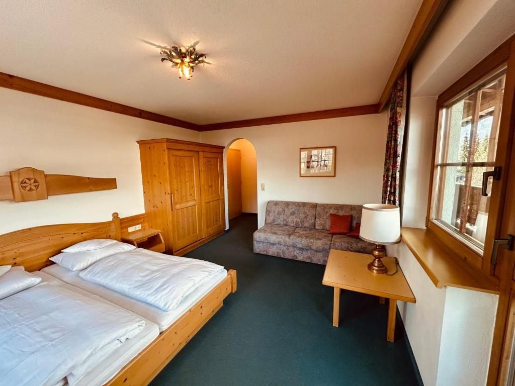 A bedroom with a wooden bed, a sofa, a small table, and a window with curtains.