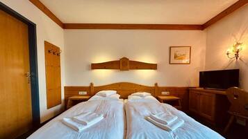 Habitación de hotel con dos camas, cabecera de madera, televisor y lámpara fijada a la pared.