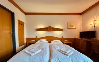 Habitación de hotel con dos camas, cabecera de madera, televisor y lámpara fijada a la pared.