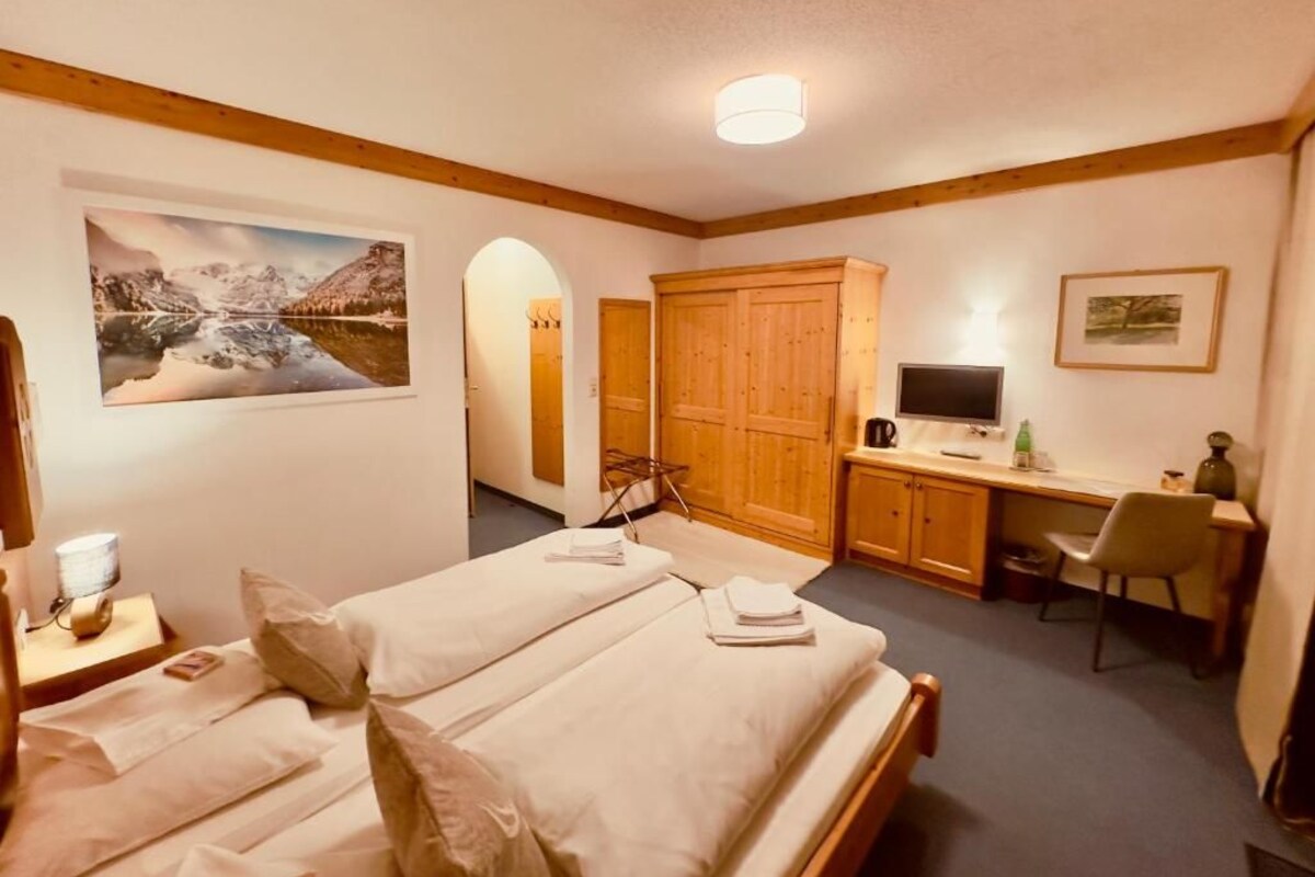 Ein Hotelzimmer mit zwei Betten, einem Schreibtisch, einem Fernseher und einem großen Fenster.
