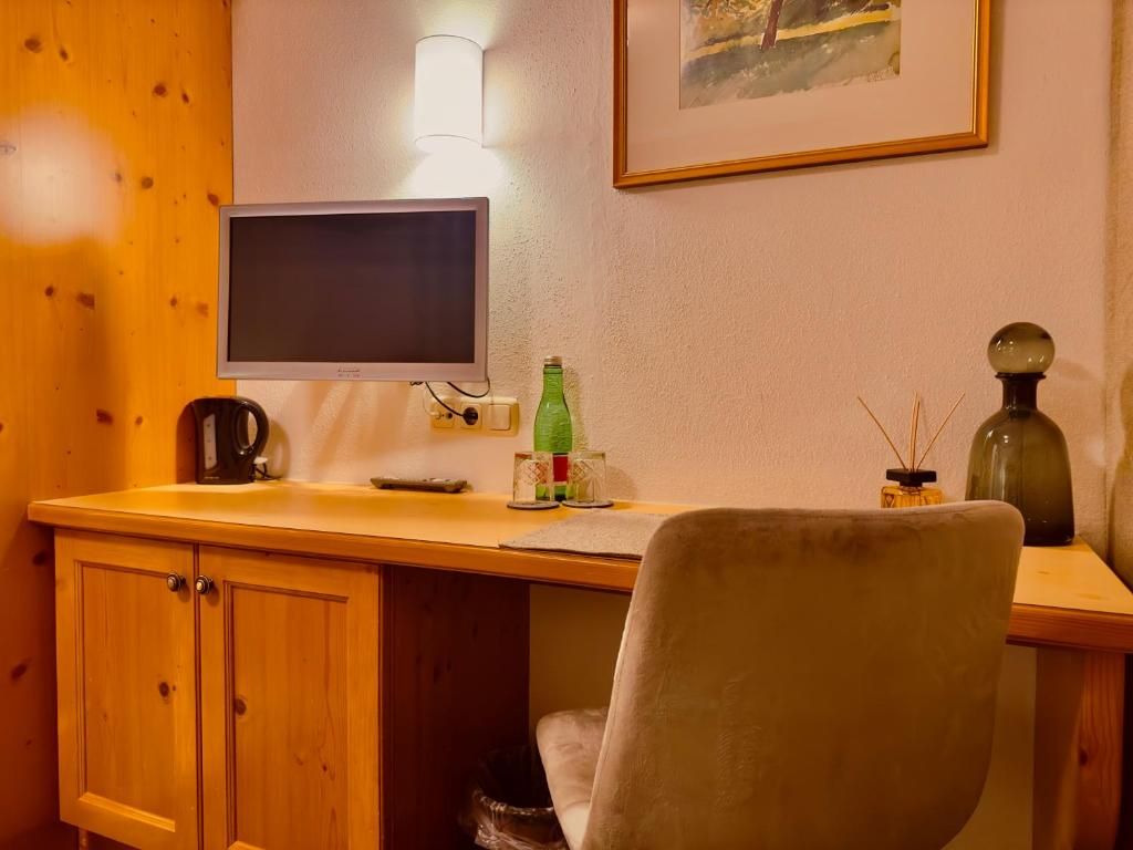 A wooden desk with a computer monitor, a green bottle, and a decorative item on the wall.