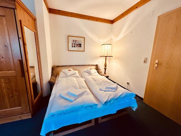 A hotel room with a bed, a wooden wardrobe, a lamp, and a door.