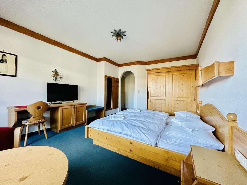 A bedroom with a wooden bed, a desk with a chair, a television, and a wardrobe.