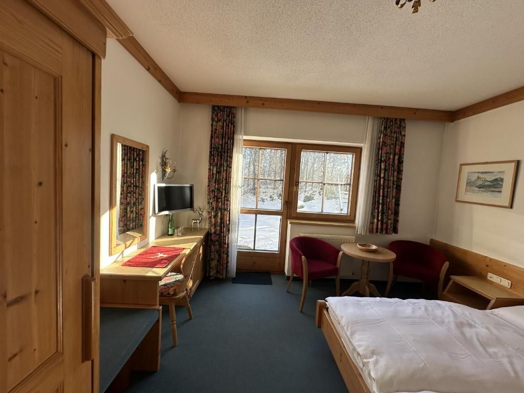Una habitación de hotel con cama, escritorio, silla, una mesita y ventana con cortinas.