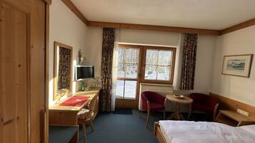 Una habitación de hotel con cama, escritorio, silla, una mesita y ventana con cortinas.