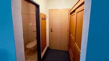 A narrow hallway with a wooden door, a visible toilet, and a blue wall.