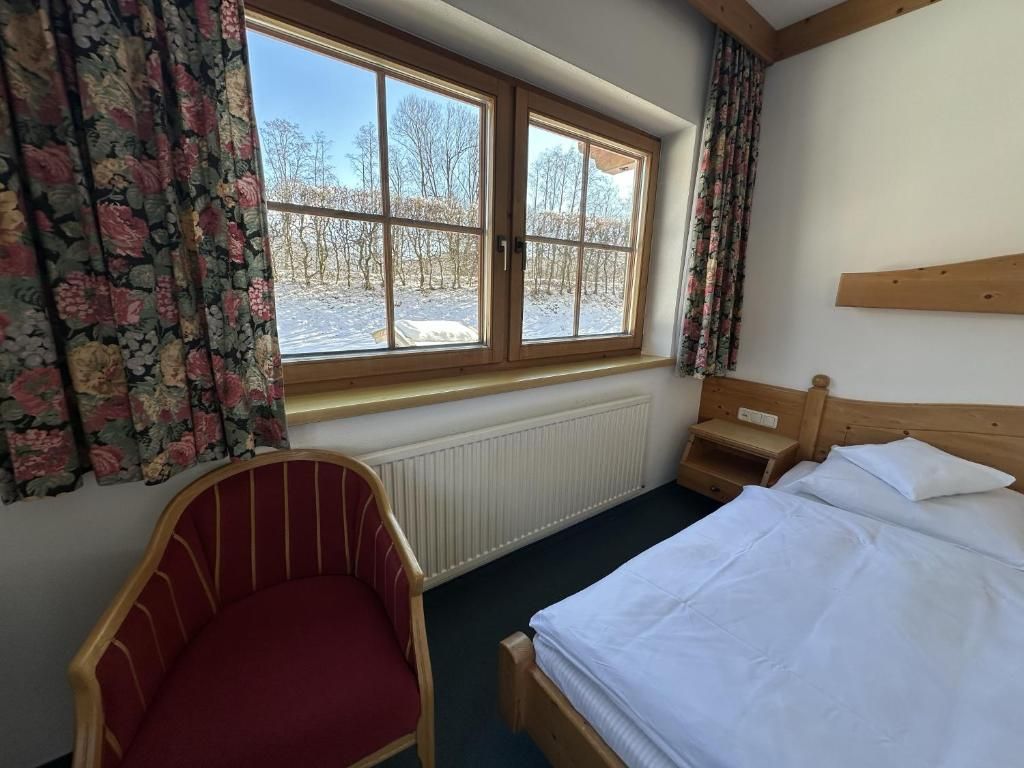 Ein Schlafzimmer mit einem Bett, einem Sessel, einem Fenster mit Vorhängen und Blick auf eine verschneite Landschaft.