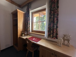 A room with a wooden desk, a chair, a window with curtains, and a small shelf with decorative items.
