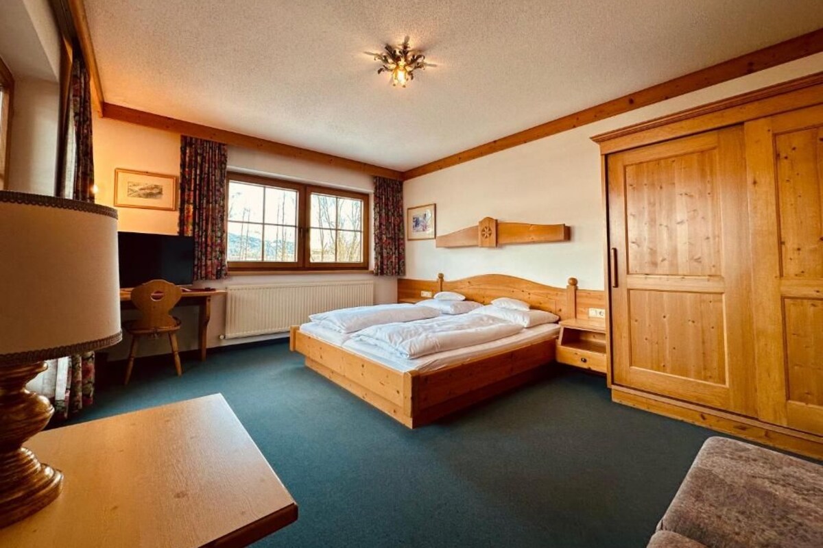 Ein Schlafzimmer mit einem hölzernen Bett, einem Schreibtisch, einem Stuhl, einem Kleiderschrank und einer Heizung.