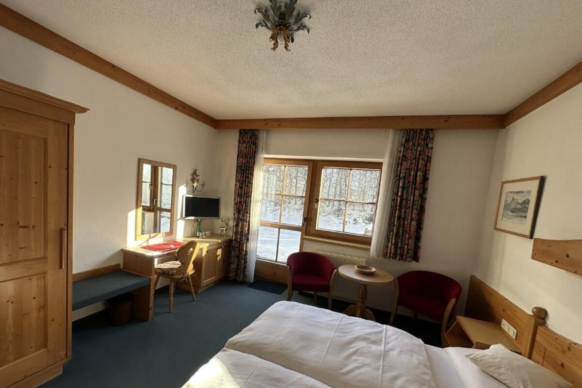 Ein Hotelzimmer mit Bett, Schreibtisch, Stuhl und einem fensterbepflanzten Fenster.