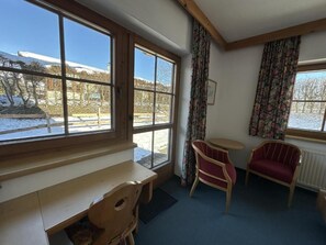 A room with a wooden bench, two chairs, a small table, and large windows with curtains.
