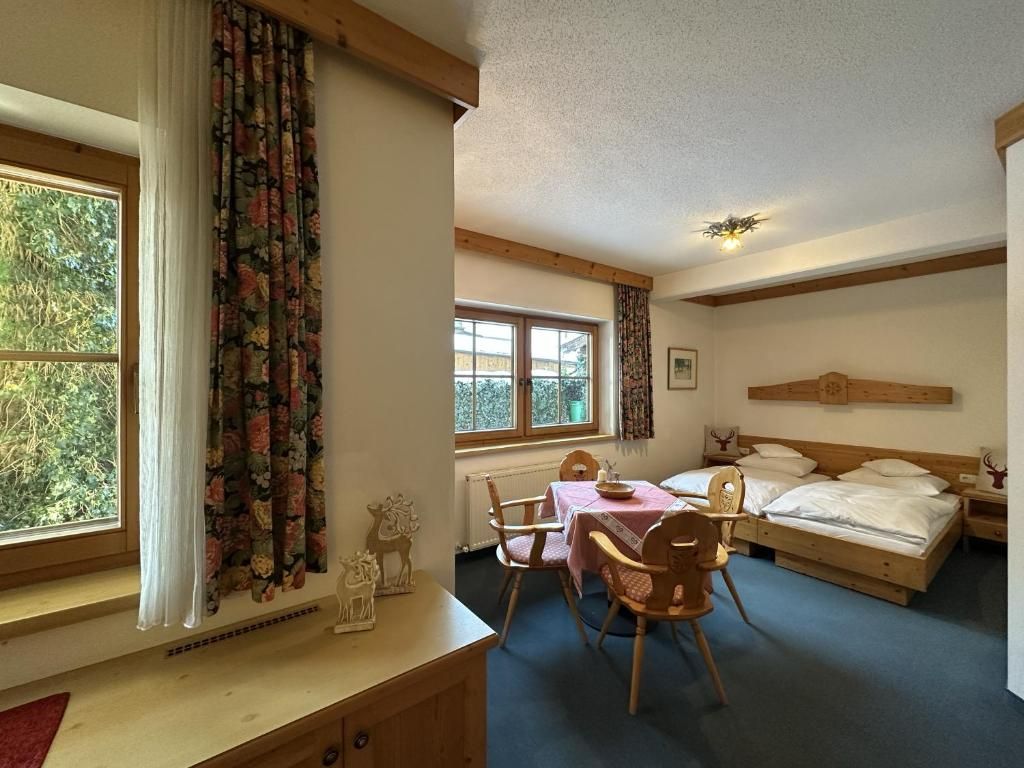 Una habitación con una cama, una mesa con sillas y un ventanal con cortinas.
