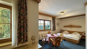 Una habitación con una cama, una mesa con sillas y un ventanal con cortinas.