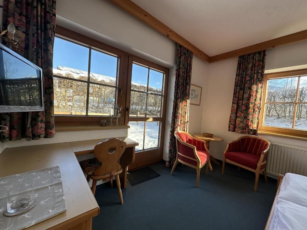 Ein Hotelzimmer mit großem Fenster, einem Holztisch, einem roten Sessel, einem Bett und einem Fernseher.