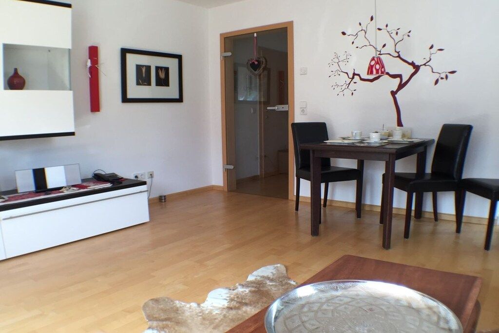 A dining area with a table and chairs, a white cabinet with a flat-screen TV, and a wall with a tree decal.