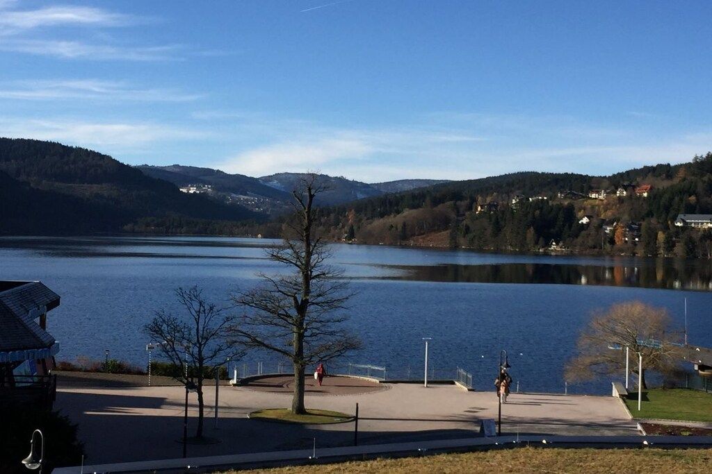 Vista sul lago con cielo sereno, un sentiero pedonale e un piccolo edificio con tetto.