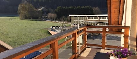 A balcony with a wooden railing overlooking a grassy field and a building in the distance.