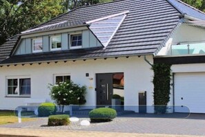 Einbungalow mit geneigtem Dach, einer Garage und einem kleinen Vorgarten mit Hecke und Blumenbeet.