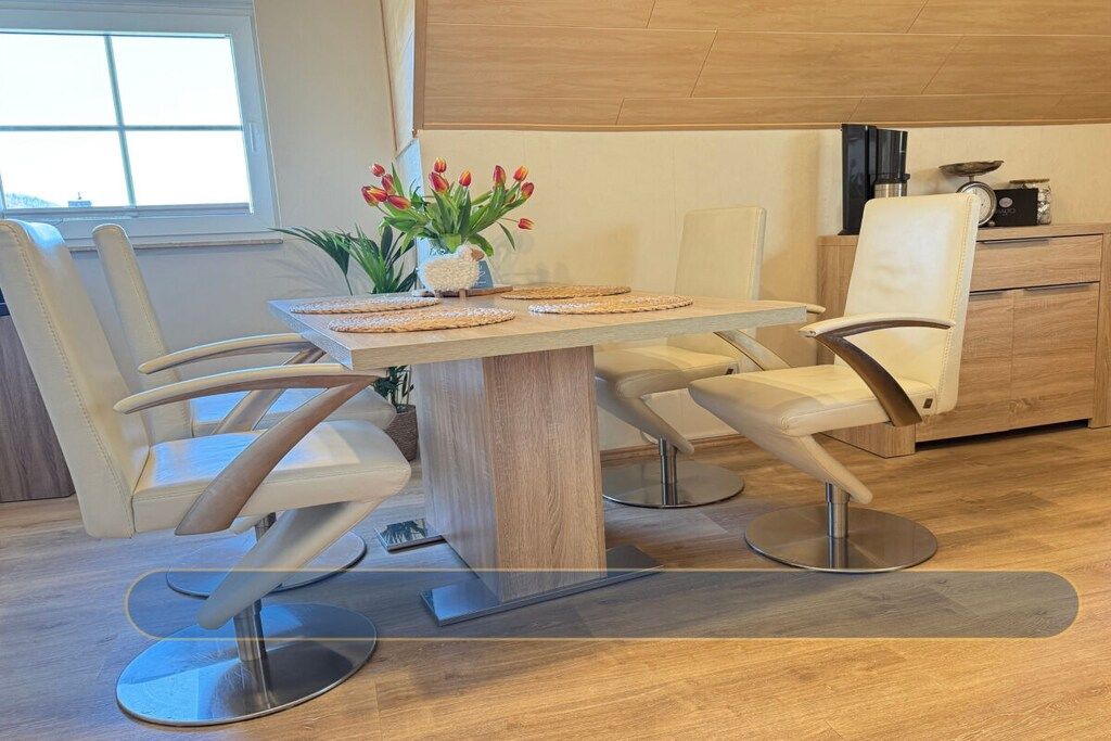 A modern dining area with a wooden table, four white chairs, and a vase with red flowers.
