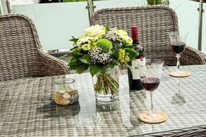 A wicker table with a glass vase of flowers, a bottle of wine, and two wine glasses. - Holiday apartment with 2 bedrooms (Bad Harzburg)