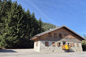A stone building with wooden shutters, surrounded by dense forest.