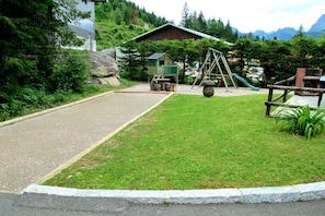 A playground with a swing set and slide, surrounded by a grassy area and a building with a sloped roof.