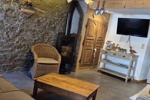 A cozy living room with a stone wall, a fireplace, a wicker chair, a wooden table, and a TV mounted on the wall.