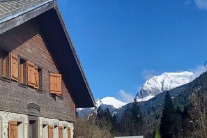 Un bâtiment en bois, doté d’un toit en pente et de volets en bois, se dressant sur fond de montagnes enneigées et d’un ciel bleu azur.