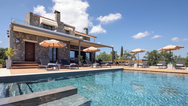 Ein moderner Poolbereich mit klarem Wasser, Steinwänden und Liegestühlen mit Sonnenschirmen.