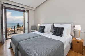 A bedroom with two beds, a balcony with a table and chairs, and a view of the sea. - Villa Nera Corfu (Kerkira)