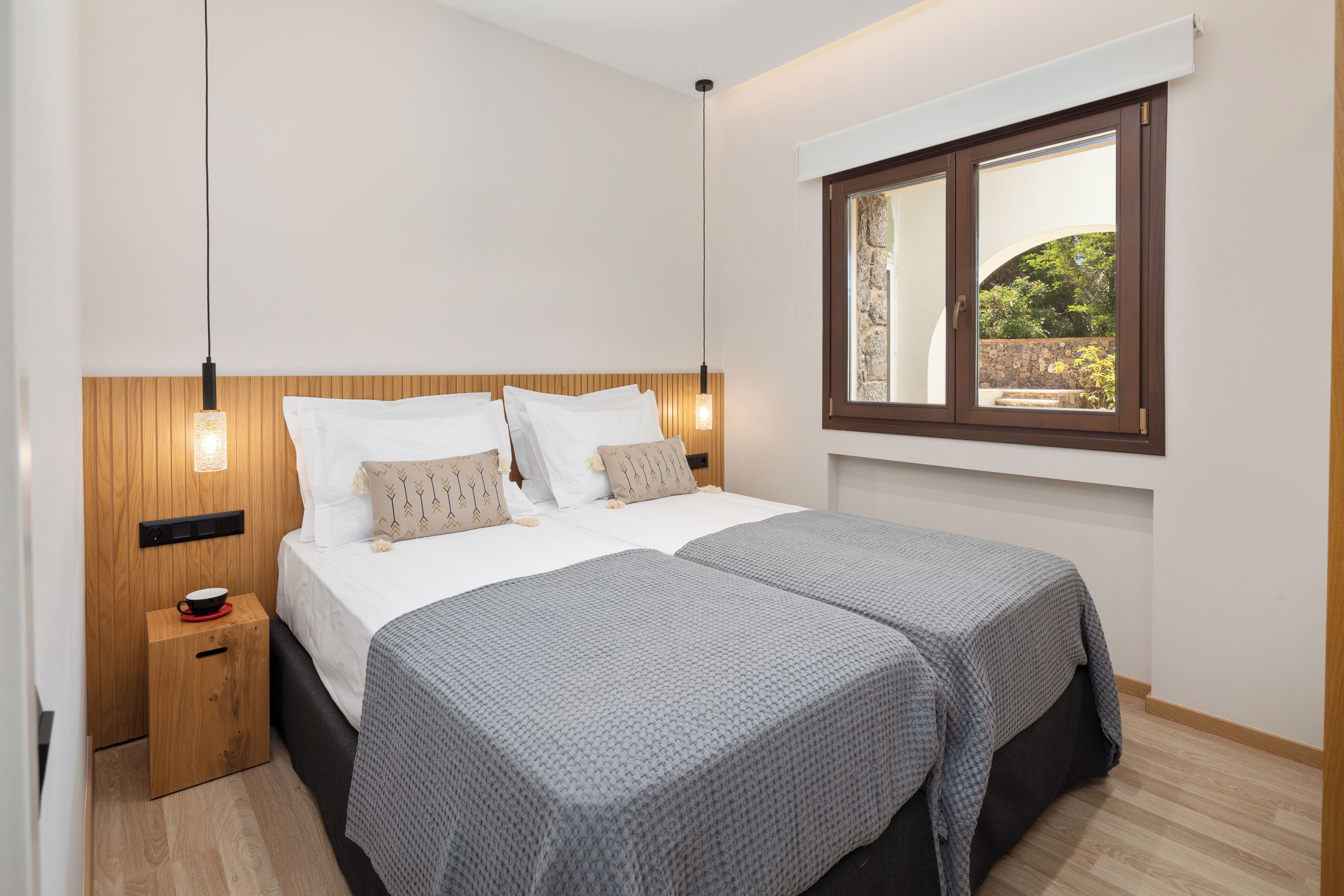Uma cama de casal com cabeceira de madeira, duas mesas de cabeceira e uma janela com vista para o verde.