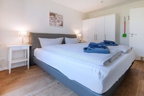 A bedroom with a bed, bedside tables, a wardrobe, and a wall-mounted picture. - Dune Star Wangerooge (Wangerooge)